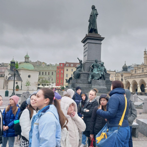 Dzieci na wycieczce w Krakowie. Stoją na rynku krakowskim. W tle pomnik Adama Mickiewicza i Sukiennice. Kliknięcie na zdjęcie spowoduje jego powiększenie do rozmiaru oryginalnego.