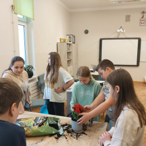 Dzieci z kl. 5 b wspólnie sadzą kwiatki doniczkowe pod nadzorem wychowawczyni.  Kliknięcie na zdjęcie spowoduje jego powiększenie do rozmiaru oryginalnego.