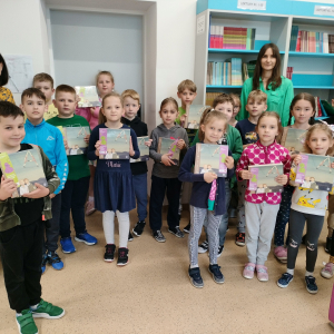 Dzieci z kl. 1 a wraz z panią Wicedyrektor Dorotą Gurgul i wychowawczynią panią Dorotą Gargul w szkolnej bibliotece. Uczestniczą we wręczaniu książek z pasowania na czytelnika. W tle regały biblioteczne. Kliknięcie na zdjęcie spowoduje jego powiększenie do rozmiaru oryginalnego.