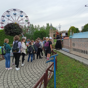 Uczestnicy wycieczki przechodzą w Parku Miniatur obok jednego z modelu. W tle Diabelski Młyn - okrągła karuzela z gondolami do siedzenia. Kliknięcie na zdjęcie spowoduje jego powiększenie do rozmiaru oryginalnego. 