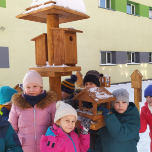 Dzieci z kl. 1 karmią ptaki w karmnikach zainstalowanych w ramach projektu "Klasa z Drewna". .  Kliknięcie na zdjęcie spowoduje jego powiększenie do rozmiaru oryginalnego.