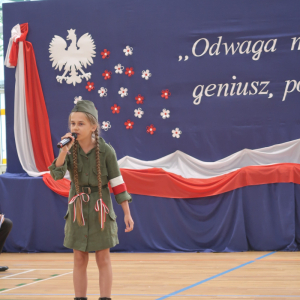 Uczennica kl. 5 a wykonuje patriotyczną piosenkę w czasie akademii z okazji rozpoczęcia roku szkolnego.  Kliknięcie na zdjęcie spowoduje jego powiększenie do rozmiaru oryginalnego.