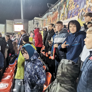 Uczestnicy wyjazdu na mecz siedzą na stadionie Wisły Kraków w otoczeniu innych kibiców. Kliknięcie na zdjęcie spowoduje jego powiększenie do rozmiaru oryginalnego.