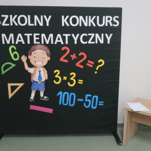 Sztaluga z dekoracjami związanymi ze szkolnym konkursem "Liczydełko".  Na sztaludze chłopiec z plecakiem oraz kolorowe działania matematyczne. Kliknięcie na zdjęcie spowoduje jego powiększenie do rozmiaru oryginalnego.