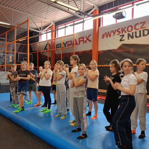 Uczniowie klas czwartych rozgrzewają się wraz z trenerką w parku trampolin. Kliknięcie na zdjęcie spowoduje je go powiększenie do rozmiaru oryginalnego.