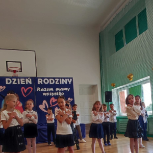 Pierwszoklasiści tańczą ze skrzyżowanymi rękami dla rodziców. Kliknięcie na zdjęcie spowoduje jego powiększenie do rozmiaru oryginalnego.