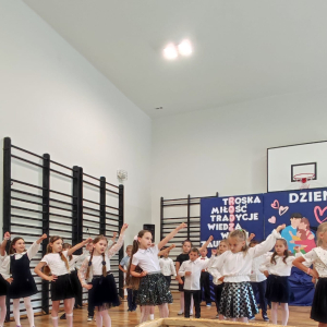 Dzieci unoszą ręce nad głowami w trakcie tańca dla rodziców. Kliknięcie na zdjęcie spowoduje jego powiększenie do rozmiaru oryginalnego.