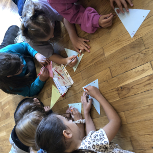 Czwartoklasiści siedzą na podłodze i przygotowują chorągiewki. Malują je pisakami. Kliknięcie na zdjęcie spowoduje jego powiększenie do rozmiaru oryginalnego.