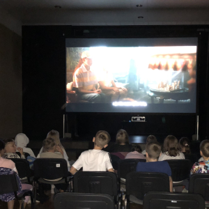 Klasy 4 a i b w trakcie oglądania filmu w Gminnym Centrum Kultury Czytelnictwa i Sportu w Szczurowej. Dzieci siedzą na krzesełkach przed nimi ekran z filmem Akademia Pana Kleksa. Kliknięcie na zdjęcie spowoduje jego powiększenie do rozmiaru oryginalnego.