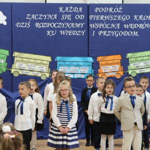 Dzieci z klas pierwszych śpiewają piosenki na pasowaniu. W tle dekoracja z pociągiem zawierającym imiona pierwszaków. Kliknięcie na zdjęcie spowoduje jego powiększenie do rozmiaru oryginalnego.