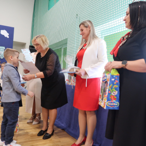 Pani Iwona Czesak wręcza dyplom jednemu z uczniów w trakcie pasowania na ucznia klas 1. Towarzyszy jej pani Dyrektor Joanna Ozorka-Krawczyk oraz przedstawicielka racy rodziców. Kliknięcie na zdjęcie spowoduje jego powiększenie do rozmiaru oryginalnego.