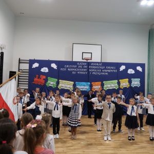 Pierwszaki w trakcie pasowania z rękami skierowanymi w stronę szkolnego sztandaru. Kliknięcie na zdjęcie spowoduje jego powiększenie do rozmiaru oryginalnego.