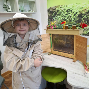 Uczeń w stroju pszczelarza obok ramka, na której pszczoły gromadzą miód. Kliknięcie na zdjęcie spowoduje jego powiększenie do rozmiaru oryginalnego.