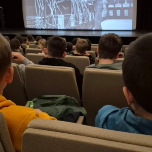 Uczniowie siedzą w fotelach, przed nimi ekran z filmem dotyczącym AI.  Kliknięcie na zdjęcie spowoduje jego powiększenie do rozmiaru oryginalnego.