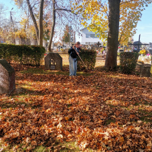 Jedna z dziewczynek grabi liście na cmentarzu obok grobów żołnierskich. Kliknięcie na zdjęcie spowoduje jego powiększenie do rozmiaru oryginalnego.