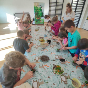 Dzieci wykonują ozdoby ze specjalnego pisaku i roślinek na warsztatach dotyczących lasu. Kliknięcie na zdjęcie spowoduje jego powiększenie do rozmiaru oryginalnego.