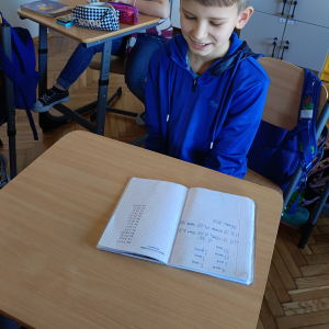 Uczeń z zeszytem zawierającym działania z mnożenia do wykonania. Kliknięcie na zdjęcie spowoduje jego powiększenie do rozmiaru oryginalnego.