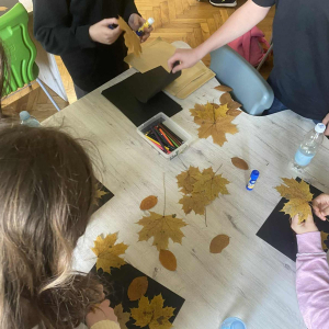 Uczniowie przyklejają liście na kartkach. Kliknięcie  na zdjęcie spowoduje jego powiększenie do rozmiaru oryginalnego.