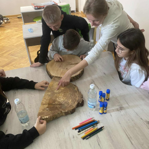 Grupka uczniów ogląda ścięte krążki drzew. Kliknięcie  na zdjęcie spowoduje jego powiększenie do rozmiaru oryginalnego.