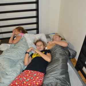 Grupka dziewczynek leży na materacach podczas nocy andrzejkowej w szkole. Kliknięcie na zdjęcie spowoduje jego powiększenie do rozmiaru oryginalnego.