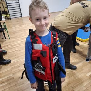 Uczeń klasy 2 w kamizelce ratunkowej przyniesionej przez strażaków. Kliknięcie na zdjęcie spowoduje jego powiększenie do rozmiaru oryginalnego.