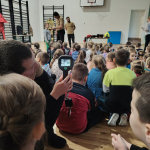 Uczniowie w trakcie patrzenia przez jedno z urządzeń przyniesionych przez pracownika straży pożarnej. Kliknięcie na zdjęcie spowoduje jego powiększenie do rozmiaru oryginalnego.