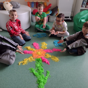 Uczniowie na zajęciach projektowych układają kwiat z kolorowych silikonowych makaronów relaksacyjnych. Kliknięcie na zdjęcie spowoduje jego powiększenie do rozmiaru oryginalnego.