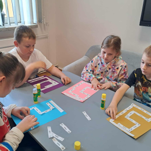 Uczniowie w trakcie przyklejania węży wyrazowych na kartkach papieru. Kliknięcie na zdjęcie spowoduje jego powiększenie do rozmiaru oryginalnego.