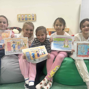 Grupka dziewczynek na pufach prezentuje prace wykonane na zajęciach projektowych. Kliknięcie na zdjęcie spowoduje jego powiększenie do rozmiaru oryginalnego.