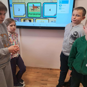 Dzieci w trakcie ćwiczeń, w tle ekran z programem multimedialnym. Kliknięcie na zdjęcie spowoduje jego powiększenie do rozmiaru oryginalnego.