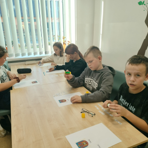 Uczniowie siedzą przy stole, biorą udział w zajęciach projektowych. Kliknięcie na zdjęcie spowoduje jego powiększenie do rozmiaru oryginalnego.