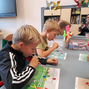 Chłopcy wykonują ćwiczenia oddechowe ze słomkami, dmuchają elementy. Kliknięcie na zdjęcie spowoduje jego powiększenie do rozmiaru oryginalnego.