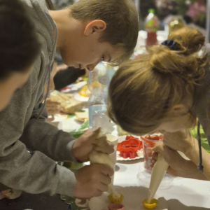 Napełnianie farszem babeczek przez siódmoklasistów. Klasa 7 b bawi się w krzesła - uczniowie chodzą wokół krzeseł. Kliknięcie na zdjęcie spowoduje jego  powiększenie do rozmiaru oryginalnego.