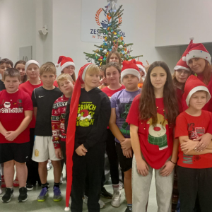 Szóstoklasiści ubrani w świąteczne stroje wraz z nauczycielami na tle szkolnej choinki.  Kliknięcie na zdjęcie spowoduje jego powiększenie do rozmiaru oryginalnego.