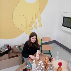 Wolontariuszka mocuje choinkę do drewnianego krążka. Kliknięcie na zdjęcie spowoduje jego powiększenie do rozmiaru oryginalnego.