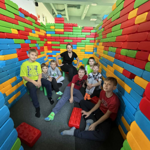 Grupka chłopców pomiędzy ścianami zbudowanymi z kolorowych klocków. Towarzyszy im pani Magdalena Małek. Kliknięcie na zdjęcie spowoduje jego powiększenie do rozmiaru oryginalnego.