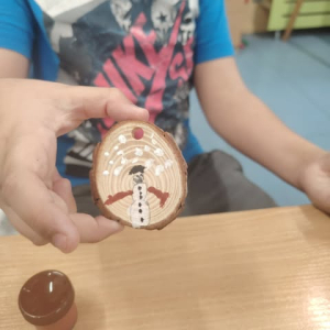 Dziecko prezentuję bombkę z bałwankiem namalowaną na drewnie. Klikniecie na zdjęcie spowoduje jego powiększenie do rozmiaru oryginalnego.