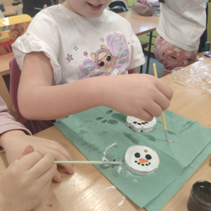 Jedna z uczennica maluje główkę bałwanka na drewienku. Klikniecie na zdjęcie spowoduje jego powiększenie do rozmiaru oryginalnego.