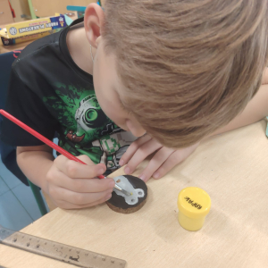 Uczeń w trakcie malowania drewnianej bombki. Klikniecie na zdjęcie spowoduje jego powiększenie do rozmiaru oryginalnego.