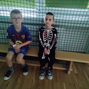 Chłopcy przebrani w stroje karnawałowe siedzą na ławce. Kliknięcie na zdjęcie spowoduje jego powiększenie do rozmiaru oryginalnego.