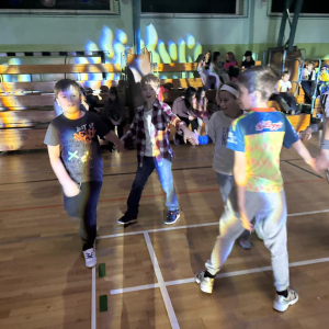 Grupka uczniów w trakcie zabawy karnawałowej na hali gimnastycznej. Kliknięcie na zdjęcie spowoduje jego powiększenie do rozmiaru oryginalnego.