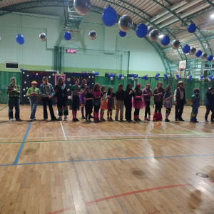 Uczniowie stoją w szeregu na hali gimnastycznej. Biorą udział w zabawie karanawałowej. Kliknięcie na zdjęcie spowoduje jego powiększenie do rozmiaru oryginalnego.