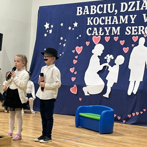 Dwójka przedszkolaków w trakcie recytacji wierszy dla dziadków.  Kliknięcie na zdjęcie spowoduje jego powiększenie do rozmiaru oryginalnego.