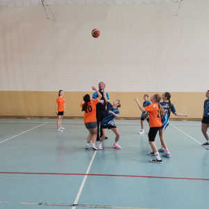 Uczennice grają w koszykówkę na zawodach.  Kliknięcie na zdjęcie spowoduje jego powiększenie do rozmiaru oryginalnego.