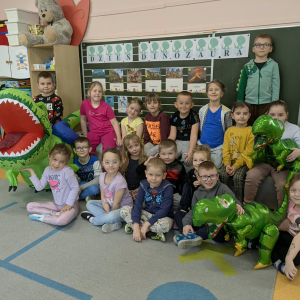 Przedszkolaki zgromadzone przy tablicy obchodzą Dzień Dinozaura. Kliknięcie na zdjęcie spowoduje jego powiększenie do rozmiaru oryginalnego.