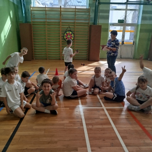 Uczniowie klasy 1 b siedzą na parkiecie na hali gimnastycznej. Kliknięcie na zdjęcie spowoduje jego powiększenie do rozmiaru oryginalnego.