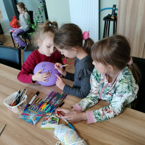 Grupka dziewczynek maluje twarz Marzanny pisakami. Kliknięcie na zdjęcie spowoduje jego powiększenie do rozmiaru oryginalnego.