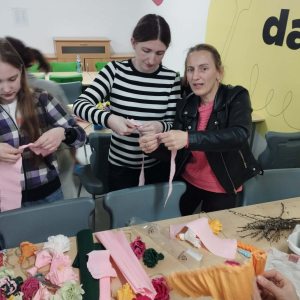 Mamy i córki skręcają kwiaty z bibuły na wielkanocną palmę. Kliknięcie na zdjęcie spowoduje jego powiększenie do rozmiaru oryginalnego.