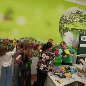 Uczniowie wraz z mamami trzymają wielką palmę wielkanocną. Kliknięcie na zdjęcie spowoduje jego powiększenie do rozmiaru oryginalnego.