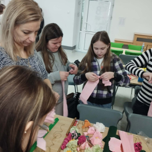 Dzieci w towarzystwie rodziców przygotowują bibułowe kwiatki na palmę wielkanocną. Kliknięcie na zdjęcie spowoduje jego powiększenie do rozmiaru oryginalnego.